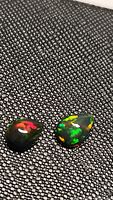Close-up view of two pear-shaped cabochon black opals with visible vibrant rainbow flashes in red, green, yellow, and orange on a textured black background.