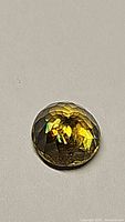 Front view of the round faceted sphene gemstone showing yellow-green color and rainbow luster under light.