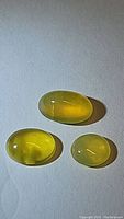 Three yellow oval cabochon African fire opal gemstones on white background.