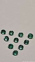 Ten round green faceted emerald gemstones on white background