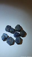 Seven natural, opaque blue sapphire rough crystals on white background showing hexagonal rough crystal shapes and variations in size.