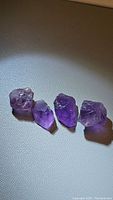 Four natural Brazilian amethyst crystals arranged side by side on a light surface, showing their size, shape, and characteristic purple color.