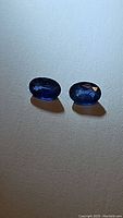 Two oval cut blue Ceylon sapphire gemstones side by side on a light textured background showing color and clarity.