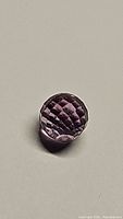 Close-up photo of a single round, sphere-shaped purple amethyst gemstone with a checkerboard faceted cut on top, showing clarity and color.