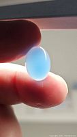 Close-up of oval, translucent lagoon blue chalcedony gemstone held between fingers showing color and translucency