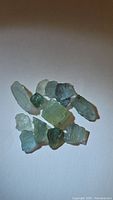 Group of 11 natural untreated aquamarine crystals in blue to greenish hues on a white background.