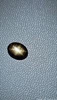Photo of oval natural black star sapphire showing six-ray golden star effect on textured gray background.