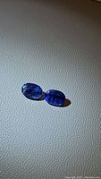 Pair of two natural blue oval cut kyanite gemstones on textured surface with visible internal inclusions.
