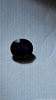 Photo of the natural oval cut blue sapphire gemstone showing its deep blue color and faceted oval shape under bright light.