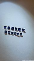 Eleven small square princess cut natural blue sapphires arranged on a white surface, showing the size and color uniformity