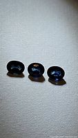 Three natural blue sapphire oval cut gemstones displayed under light, showing their deep blue color and oval faceted shapes.