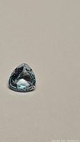 Natural sky blue topaz gemstone in trillion cut showing facets and light reflection on neutral background.