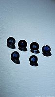 Photo showing six loose natural deep royal blue round cut sapphires arranged in two rows on a white surface.