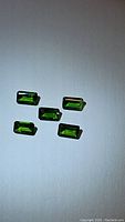 Five natural emerald cut electric green chrome diopside gemstones arranged on a white background, showing color, cut and clarity.