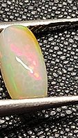 Close-up photo of a cushion cabochon cut Ethiopian opal showing pink and green rolling flashes on black textured background.