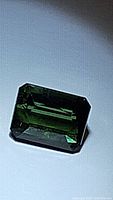 Close-up photo of a natural green tourmaline gemstone octagon cut lying flat on a surface, showing deep green color and cut facets