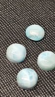 Four round natural Larimar cabochon stones on a dark fabric background.