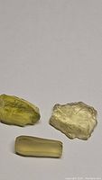 Three natural lemon citrine crystals on a white background: two rough crystalline pieces and one faceted tubular piece.