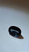 Oval cut London blue topaz gemstone displaying deep blue color and very clear clarity on light background.