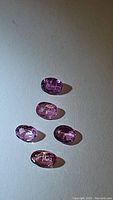 Five oval-shaped, natural cotton candy pink sapphires arranged on a flat surface, evenly spaced.