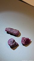 Three natural rough ruby crystals on a beige surface, clearly showing size and texture.