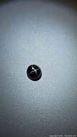 Photo of a single round black star diopside cabochon gemstone showing a white cross star pattern on top, on a grey textured background.