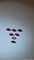 Seven marquis cut ruby gemstones displayed on a flat surface, colors varying from pink to red with purple hues visible under light