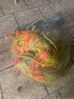View of the transparent plastic bag containing several yellow polypropylene rope bundles tied with orange marker ribbons, placed on a patterned floor.