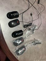 Five wired computer mice laid out on a surface, including three black Lenovo mice with red scroll wheels and two Asus mice still in plastic packaging, visible USB connectors