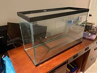 Front and side angle view of the large rectangular glass fish tank on a wooden surface, showing its transparent clean glass and black trim.