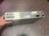 Top angled view showing metal casing, various connectors, and hand holding the unit to show size.