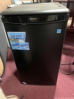 Front closed view of black Danby mini fridge with stickers on door.