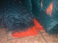 Close-up of tightly rolled green plastic snow fencing with orange edges stacked together.