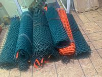10 rolls of green plastic snow fencing with orange tags, stacked side by side on plywood floor.