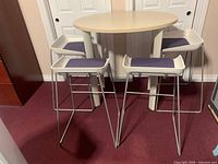 Front view of round lunchroom table and four stools showing light wood table and stools with purple cushions.