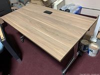 Full view of the rectangular rolling and folding table with laminate wood finish surface and metal frame on casters.