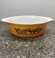 Side view of the Pyrex orange casserole dish showing the black fruit design on orange background and the white interior rim.