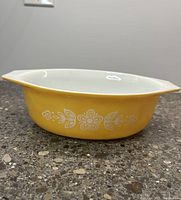 Side view of Pyrex casserole dish showing orange daisy design, two small handles, and white interior.