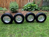 Four 15x7J ET 49 alloy rims with mounted Winterforce winter tires arranged on grass, showing overall condition.