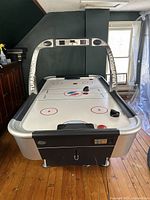 Front view of air hockey table showing full playing surface, scoreboard arch with 'Turbo Hockey' logos, four black pucks placed on the surface, and two black pushers at each side.