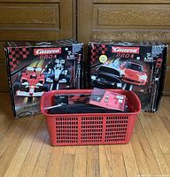 Two boxed Carrera Pro-X digital racing sets and red basket with manuals and track parts on wood floor.