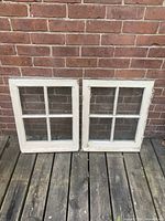 Photo of two wooden framed windows with four glass panes each, showing front view against a brick wall
