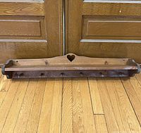 Front view of wooden wall shelf showing heart cutout and seven wooden pegs on natural wood finish.