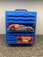 Front view of blue plastic Hot Wheels rolling case with embossed cars and display compartment showing one Hot Wheels car and original label