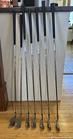 Full view of 7 golf irons showing length and grips, arranged upright.