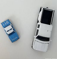 Top-down view of both models, showing the white Chevrolet pickup truck with black bed and blue Chevrolet police car side by side on a white background.