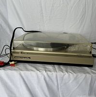 Side view of the Marantz TT 1060 turntable showing the clear plastic dust cover, Marantz label on front, and attached audio cables.