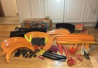 Wide view showing a large assortment of orange, black, yellow, red, and purple Hot Wheels track parts spread on the floor. The Sizzlers Laguna Oval Set box is visible in background.