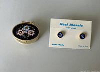 Photo of the closed hinged box with floral mosaic on top and the pair of small mosaic stud earrings on a card.