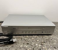 Front view of silver Norcent DP300 player with power cord laid beside on granite countertop.